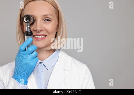 Glücklicher Dermatologe mit Dermatoskop auf grauem Hintergrund. Leerzeichen für Text Stockfoto