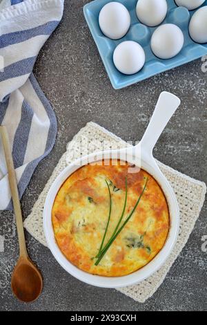 Frisch gebackene Spinat-Quiche in Keramik-Pfanne mit Eiern in blauer Eierkiste, Holzlöffel und gestreiftem Geschirrtuch. Konzept für gesunde Ernährung. Vertikales Format Stockfoto