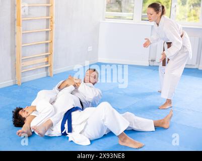 Judo- oder Jiu-Jitsu-Kurse: Zwei Männer üben das Greifen und Werfen auf Sportmatten unter der Leitung des Trainers Stockfoto