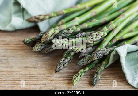 Ein Haufen frisch geernteter Spargelspeere ist ordentlich auf einem rustikalen Holztisch angeordnet, deren Grün- und Violettöne dezent durch die sanfte Note hervorgehoben werden Stockfoto