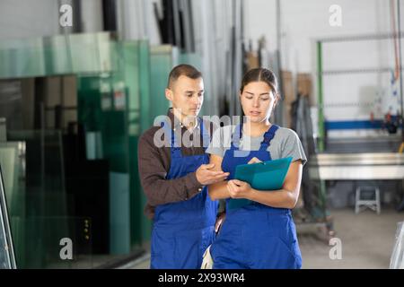 Werkstattarbeiter aus Glas diskutieren Inventarergebnisse mit Clipboard Stockfoto