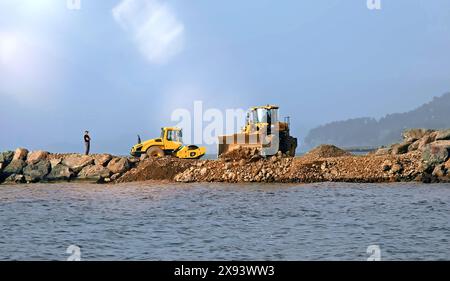 Wellenbrecherbau an der Seeküste. Der Bagger schiebt Steine an den Rand des Wassers. Problemumgehung. Batumi, Georgien. Hochwertige Fotos Stockfoto