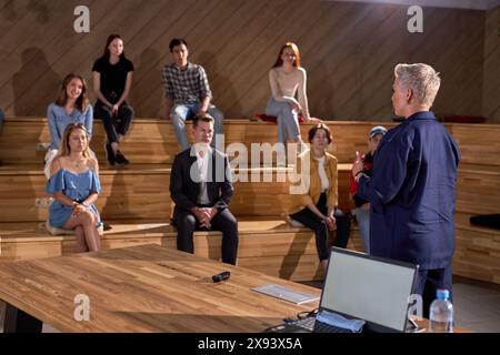 Weibliche Finanz-Coach-Gesten bei Konferenzen oder Foren. Die Studenten in einem großen Auditorium hören sich Vorlesungen an und stellen Fragen. Weibliche Sprecherin in f Stockfoto