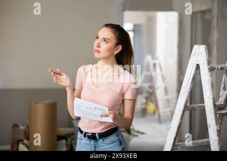 Frau überprüft den Plan des Hauses, das gerade renoviert wird Stockfoto