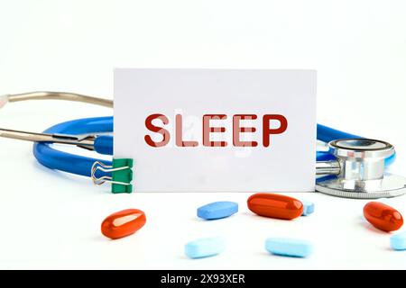 Symbol für tiefen Schlaf. Wort SCHLAF auf einer Visitenkarte neben einem Stethoskop mit Pillen und Vitaminen Stockfoto