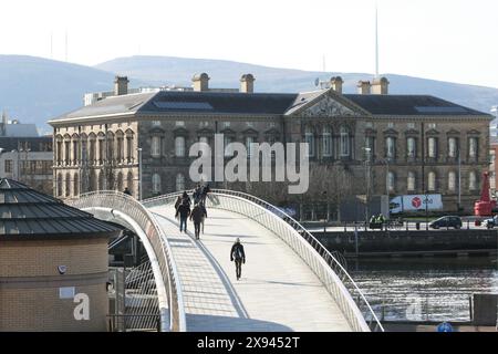 Fußgänger, die an einem sonnigen Nachmittag über die Fußgängerbrücke des Lagan Weir in Belfast laufen. Stockfoto