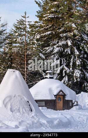 Schneebedeckte Hütte in einem lappland-Wald mit hohen Bäumen, die die ruhige Schönheit einer Winterlandschaft zeigt. Stockfoto