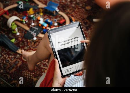 Paris, Frankreich - 11. Juni 2023: Eine Frau sitzt und surft auf einem iPad auf der Apple-Website und sieht sich die Vision Pro Produktseite mit dem Slogan „das ultimative Theater“ an. Wo auch immer Sie sind, umgeben von Kinderspielzeug auf dem Boden Stockfoto