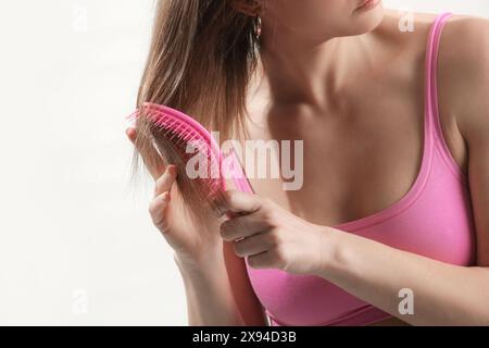 Rückansicht einer brünetten Frau, die ihr Haar mit rosa Plastik entwirrenden Haarbürste kämmt. Stockfoto