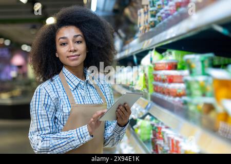Ein Supermarktmitarbeiter mit einem Tablet in der Hand, der die Produkte in den Regalen des Gangs bearbeitet und verwaltet. Stockfoto
