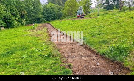 Bagger baut neuen Bürgersteig im Park. Bagger arbeitet mit breitem Löffel Stockfoto