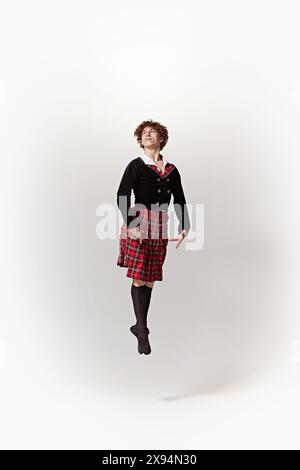 Junger Mann, Balletttänzer in traditionellem schottischem Outfit, schlägt anmutige Posen in der Luft vor weißem Studiohintergrund. Stockfoto