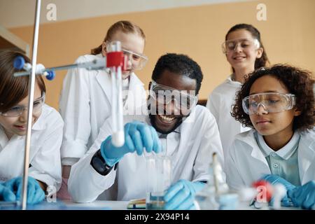 Fröhlicher afroamerikanischer Lehrer und Gruppe ethnisch vielfältiger Kinder, die Laborexperimente während des Chemiekurses machen Stockfoto
