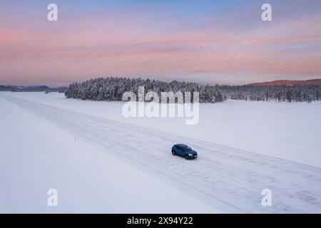 Aus der Vogelperspektive eines Autos, das auf einer vereisten Straße auf einem gefrorenen See fährt, umgeben von Nadelwäldern, in der Abenddämmerung, Jokkmokk, Schwedisch Lappland, Schweden Stockfoto