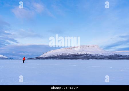 Der Mensch in der arktischen Landschaft spaziert auf der eisigen Oberfläche eines Sees vor dem Hügel Saana, Kilpisjarvi, Gemeinde Enontekio, Finnisch Lappland, Finnland Stockfoto