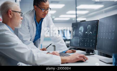Medizinisches Krankenhaus: Glücklicher Neurologe und Neurochirurg sprechen, Computer verwenden, Patient MRT Scan analysieren, Gehirn diagnostizieren. Brain Health Research Clinic: Zwei lächelnde Ärzte schauen sich CT Scan an und finden Behandlung Stockfoto
