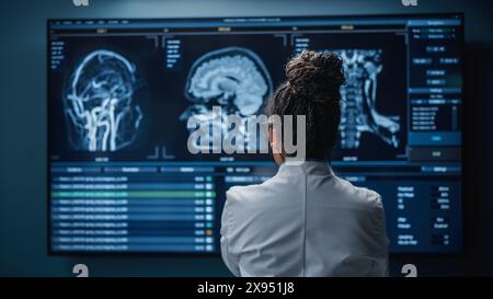 Medical Hospital Research Lab: Schwarze weibliche Neurowissenschaftlerin, die auf den TV-Bildschirm schaut, Gehirn-Scan-MRT-Bilder analysiert, Behandlung für Patienten findet. Gesundheitsneurologe, Der Menschen Heilt. Zoom Der Rückansicht Stockfoto