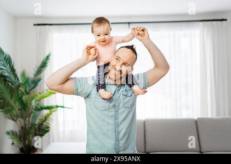 Vater mit seiner kleinen Tochter auf der Schulter, die im Wohnzimmer lustig war Stockfoto