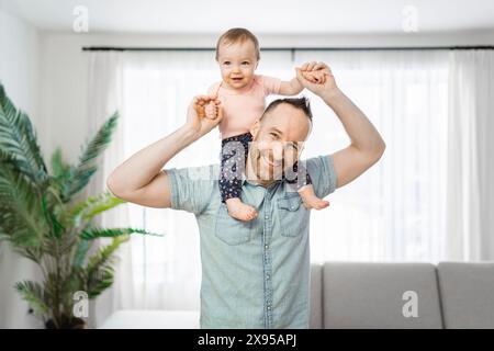 Vater mit seiner kleinen Tochter auf der Schulter, die im Wohnzimmer lustig war Stockfoto