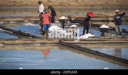 Ein Salzbauern erntet Salz unter der heißen Sommersonne. Dorfbewohner, die auf Salzfarmen in Vietnam arbeiten. Hart arbeitende Männer. Mai 8,2024 Stockfoto