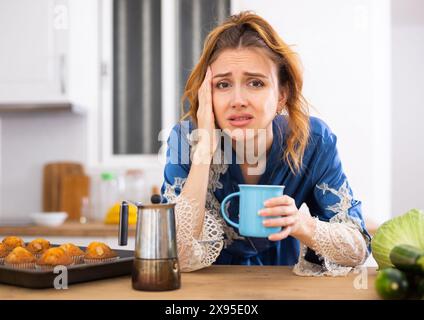 Junge Frau, die an Migräne leidet, Kaffee in der Küche trinkt Stockfoto