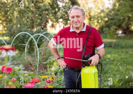 Lächelnder, entspannter älterer Mann, der Blumen im Garten sprüht Stockfoto