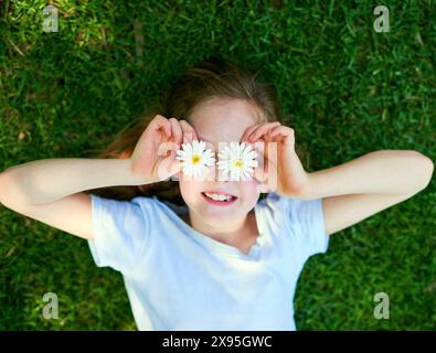 Blume, Augen und Mädchen auf dem Grasfeld mit Spaß von oben, Abenteuer und Spiel auf Entdeckungsreise, Reise oder Landschaft. Daisy, Gesicht und Happy Stockfoto