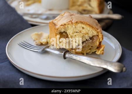 Ein Stück Biskuitkuchen auf einem hellen Teller mit Vintage-Gabel auf schwarzem Hintergrund mit dunkelblauen Vorhängen in natürlichem Licht Stockfoto