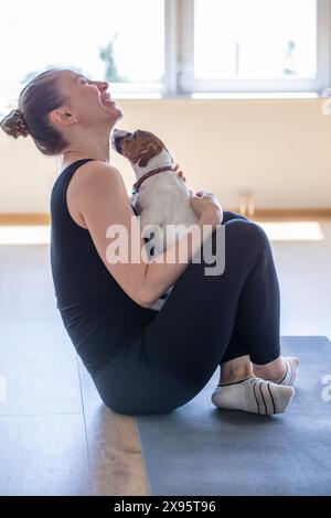 Glückliches Mädchen, Yoga, kleiner Jack Russell Terrier Welpe, Zimmer, offenes Fenster, gesunder Lebensstil, Meditation, Sport, Entspannung, Binden, Fitness, m Stockfoto