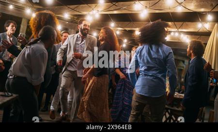 Schöne unbeschwerte Freunde tanzen zusammen und feiern ein Abendfest bei einer Party . Verschiedene multiethnische junge Erwachsene haben Spaß bei einer Firmenfeier in einem Restaurant. Stockfoto