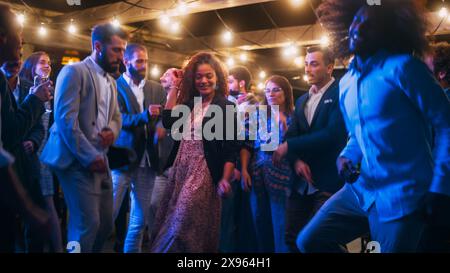 Schöne unbeschwerte Freunde tanzen zusammen und feiern ein Abendfest bei einer Party . Verschiedene multiethnische junge Erwachsene haben Spaß bei einer Firmenfeier in einem Restaurant. Stockfoto