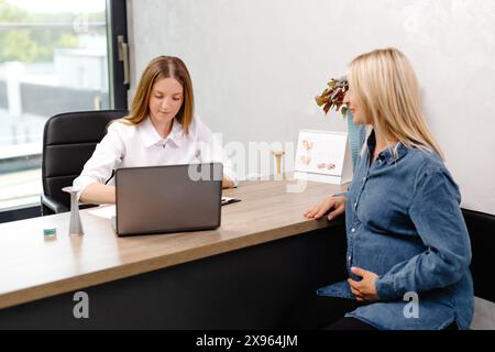 Eine junge, schwanger Frau besucht ihren Gynäkologen in der Klinik, sie sitzt auf einem Stuhl und spricht mit ihrem Arzt Stockfoto