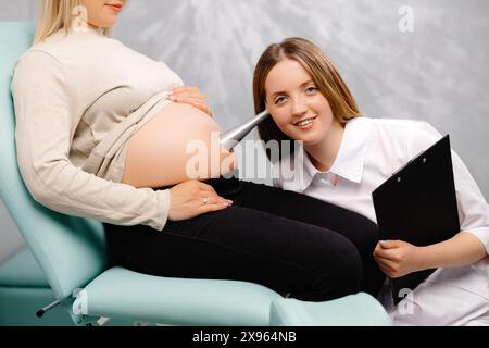 Ein Gynäkologe lehnt ein Stethoskop an den Bauch einer schwangeren Frau und hört auf den Herzschlag des Babys. Stockfoto