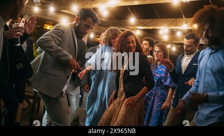 Schöne unbeschwerte Freunde tanzen zusammen und feiern ein Abendfest bei einer Party . Verschiedene multiethnische junge Erwachsene haben Spaß bei einer Firmenfeier in einem Restaurant. Stockfoto