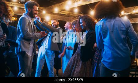 Schöne unbeschwerte Freunde tanzen zusammen und feiern ein Abendfest bei einer Party . Verschiedene multiethnische junge Erwachsene haben Spaß bei einer Firmenfeier in einem Restaurant. Stockfoto