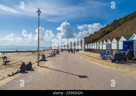 Bournemouth, Großbritannien - 30. März 2024: Menschen sitzen vor Strandhütten und sitzen am Strand von Middle Chine Beach. Stockfoto