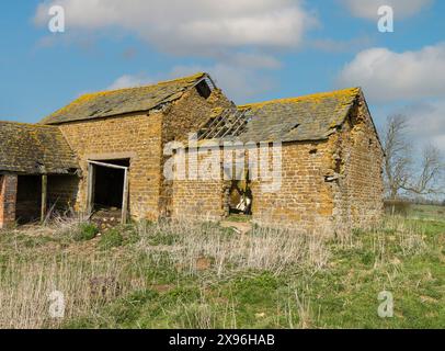 Alte ruinierte Bauernscheune aus rotem Backstein mit beschädigtem Schieferdach mit Löchern und fehlenden Schiefern, Leicestershire, England, Großbritannien Stockfoto