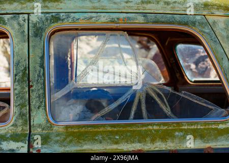 Nahaufnahme eines zerbrochenen Seitenfensters eines Oldtimers mit einem komplexen Netz aus Rissen und fehlenden Glasstücken. Stockfoto