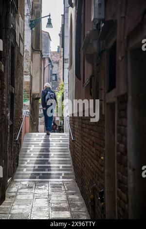 Ein einzelner Mann, der die engen Gassen entlang und die Stufen einer Brücke hinauf läuft, in Venedig Italien Stockfoto