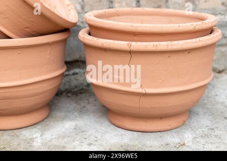 Crackederracotta Blumentopf. Ein sichtbarer Riss, der an seiner Seite läuft. Die Töpfe sind auf einer Betonoberfläche mit einer Ziegelwand im Hintergrund gestapelt. Stockfoto