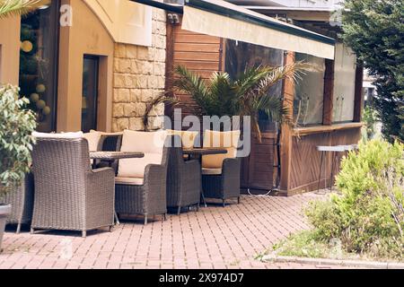 Rattan Korbmöbel, Stühle und ein quadratischer Tisch stehen an einem sonnigen Tag auf einem Fußgängerdamm nahe einem Café im Freien am frühen Morgen ohne Menschen. Mit Platz zum Kopieren. Hochwertige Fotos Stockfoto