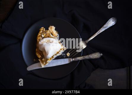 Tischfotografie von einem Stück Pavlova-Meringue-Kuchen mit Kaffeesauce und Walnüssen auf einer schwarzen Keramikplatte mit Vintage-Gabel und Kni Stockfoto
