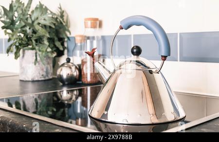 Ein stilvoller Wasserkocher aus Edelstahl mit silbernem Pfeifen auf einem schwarzen Keramikkochfeld und einer Arbeitsfläche in einer hellen, modernen Wohnwohnung oder einem Wohnhaus in Großbritannien. Stockfoto