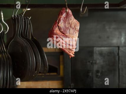 Fleischstück auf einem Haken mit Pfannen auf dem Hintergrund eines großen schwarzen Herds Stockfoto