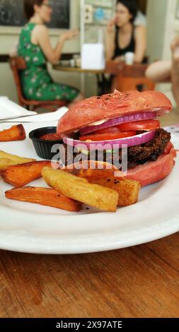 Nahaufnahme eines veganen Hamburger-Gerichts in einem roten Brötchen und Pommes Frites Stockfoto