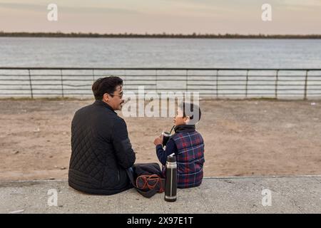 Porträt eines jungen Sohnes mit seinem Vater, der am Fluss in Argentinien plaudert und trinkt Stockfoto