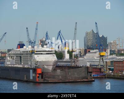 Ein großes Schiff im Hamburger Hafen mit Kränen und dem Konzertsaal der Elbphilharmonie im Hintergrund, eine große Stadt am Fluss mit Stockfoto