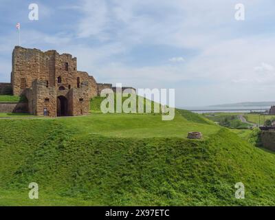 Alte Burgruinen auf einem grasbewachsenen Hügel unter blauem Himmel an einem sonnigen Tag, alte Ruinen am Meer im Grünen, Newcastle, England, Großbritannien Stockfoto