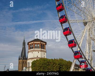 Kirchturm und historisches Gebäude neben einem Riesenrad mit roten Gondeln unter bewölktem Himmel, Riesenrad mit roten Gondeln auf einem Fluss neben einem Stockfoto