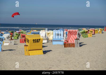 Bunte Liegestühle am Sandstrand, ein roter Drachenflieger, ruhige Meereslandschaft unter klarem Himmel, Sommerabend am Strand mit grünen Dünengräsern Stockfoto